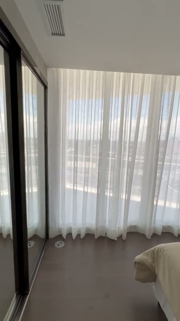 White sheer curtains framing a bedroom window beside a panelled accent wall