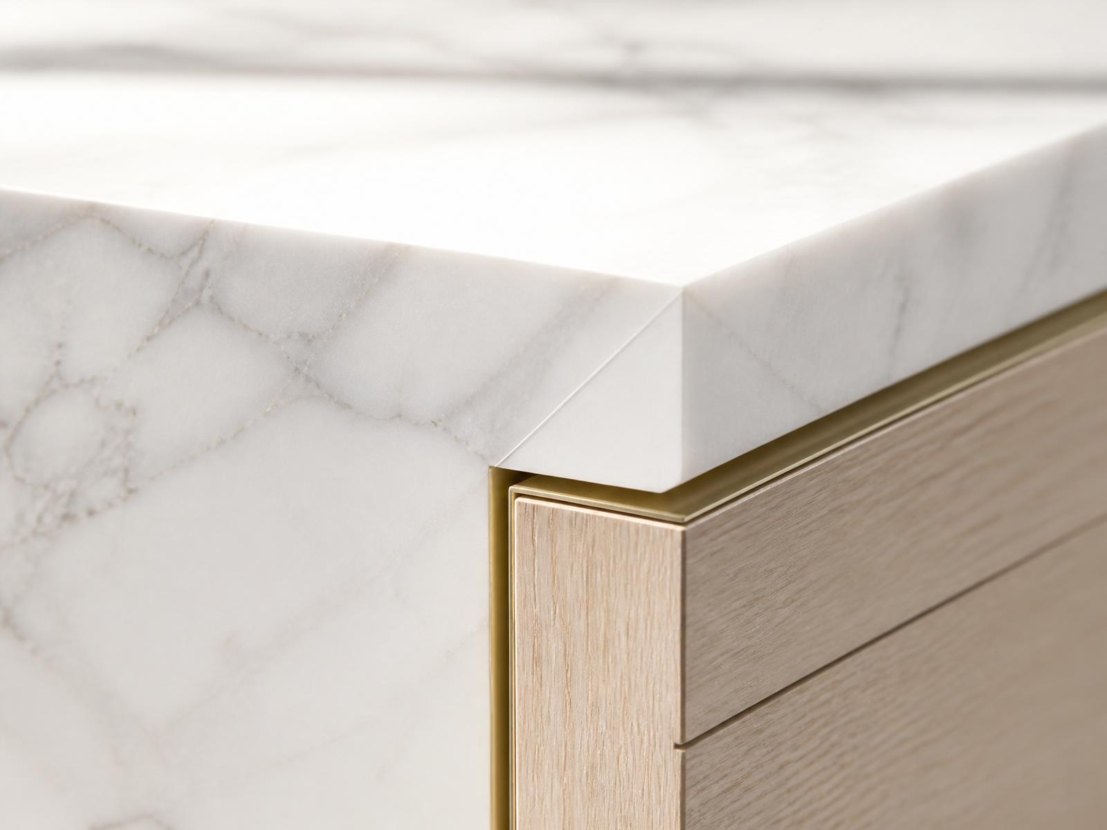 Close-up of a mitered white marble island edge with brass detail